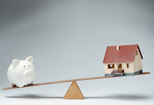 piggy bank on see-saw with model of house 